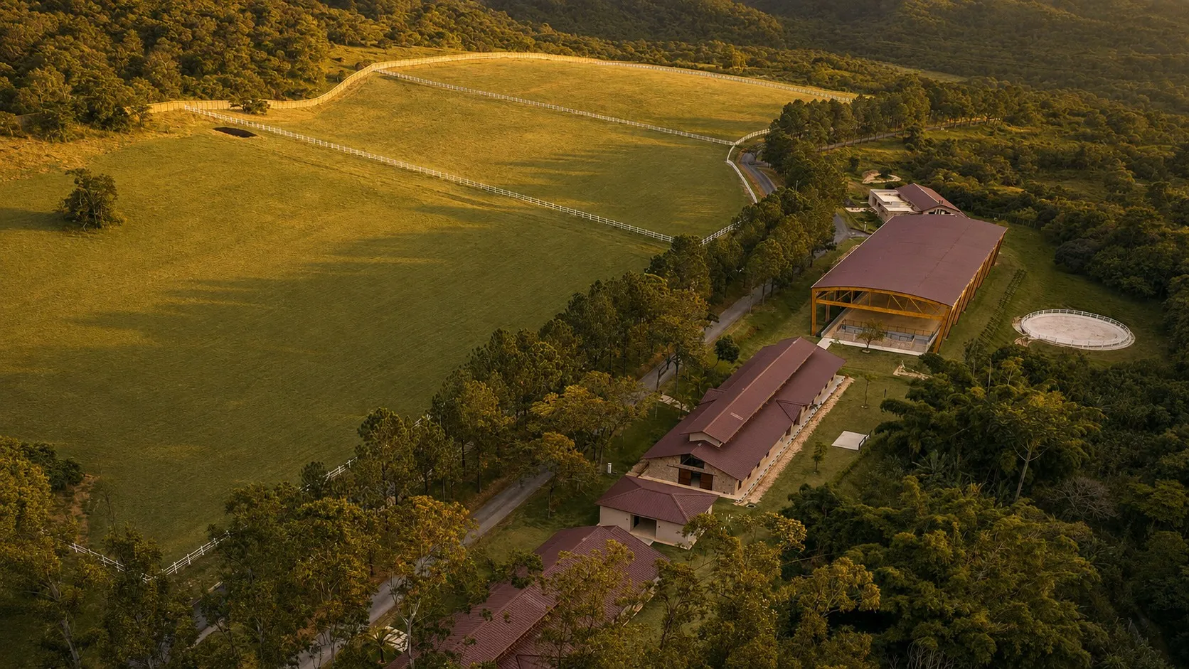 Vista aérea do centro equestre: picadeiro coberto, cocheiras, redondel e o pasto de cerca branca