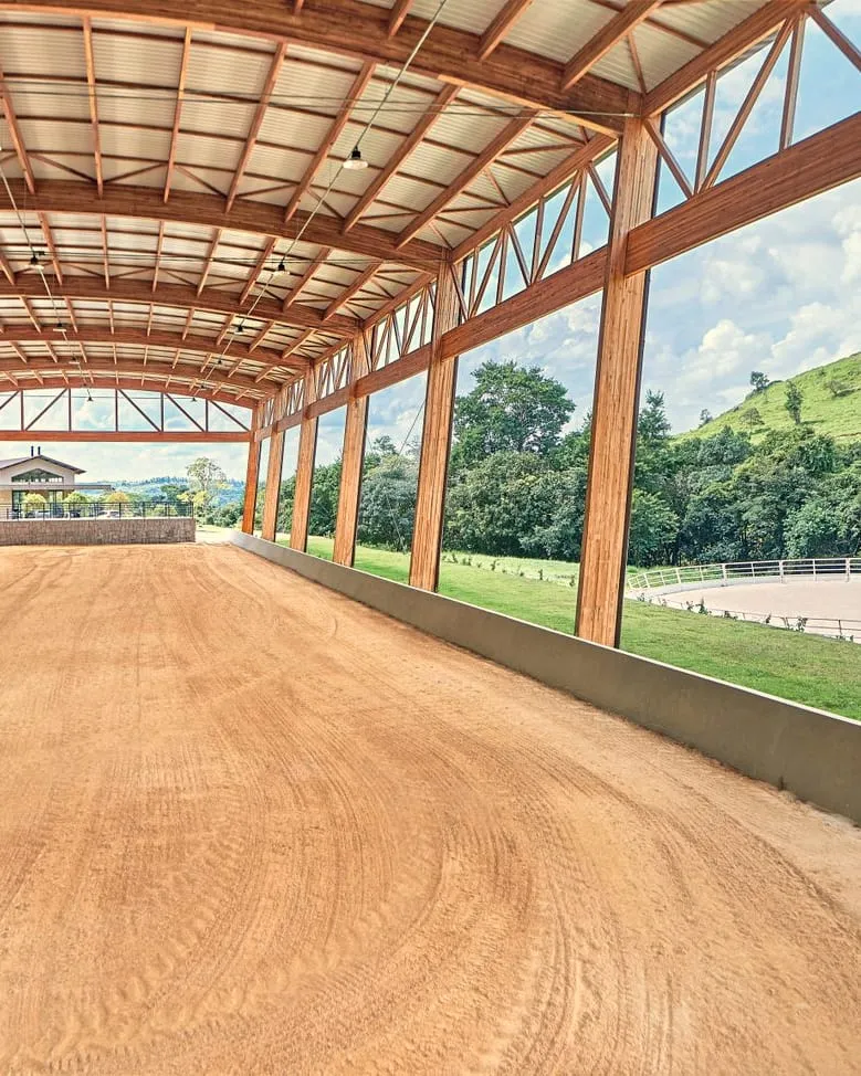 O picadeiro coberto do centro equestre, com estrutura de madeira e vista para as pistas e o vale