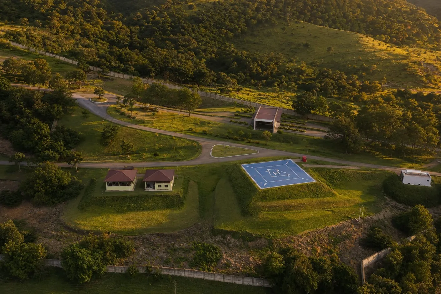 Vista aérea do heliponto e das construções de apoio, com a via de acesso passando entre eles e a mata em volta