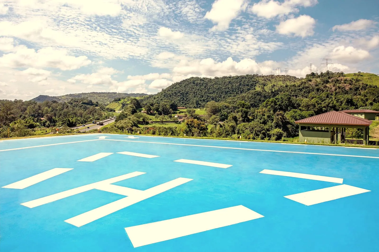 O piso do heliponto em primeiro plano, com a marcação branca, e o vale com a mata ao fundo