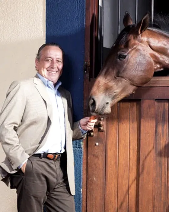 Eduardo da Rocha Azevedo à porta de uma baia, oferecendo uma cenoura a um cavalo